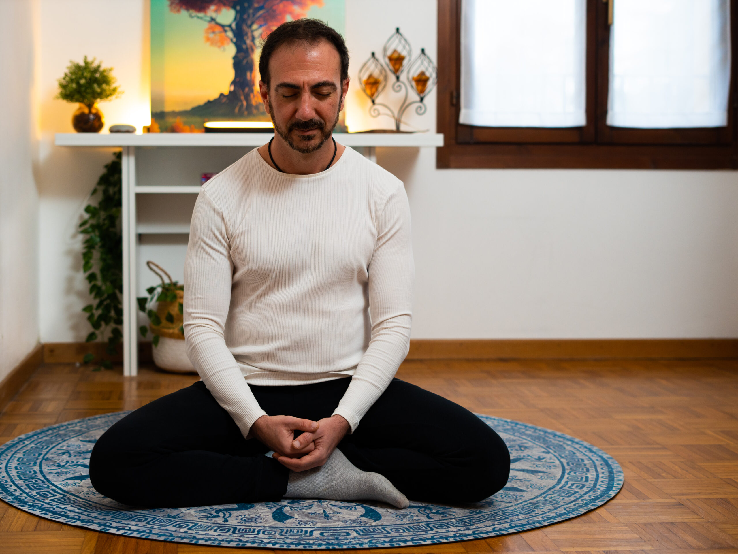 Matteo Magnano seduto a gambe incrociate su un tappeto blu mentre pratica meditazione in una stanza accogliente e rilassante.