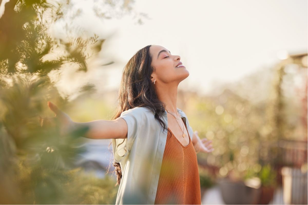 Una donna sorridente che non si sente più condizionata dal dolore, con le braccia aperte, immersa nella natura e nella luce del sole, simbolo di libertà e serenità attraverso la mindfulness.